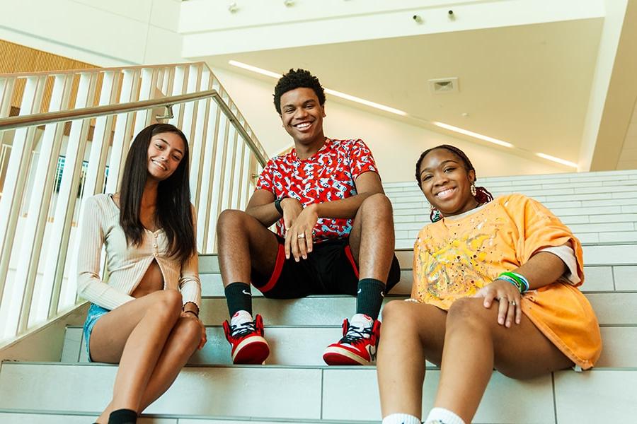 Three UMass Boston students smiling and sitting on the steps in the Integrated Sciences Complex